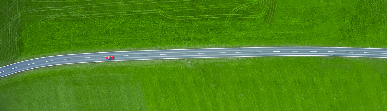 Blick aus der Vogelperspektive auf eine Landstraße, auf der ein Fahrzeug fährt