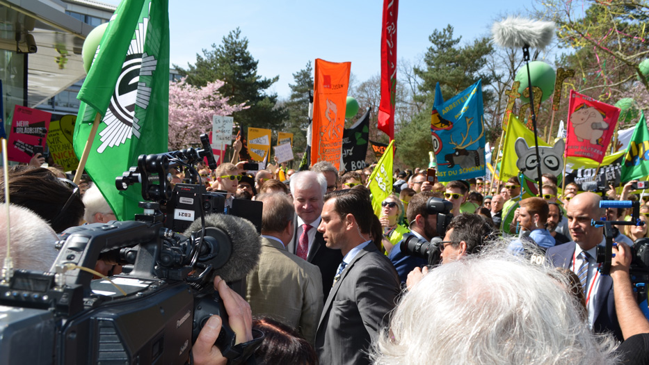 Bundesinnenminister Seehofer in mitten einer Gruppe von Personen mit Plakaten, auf denen Forderungen stehen