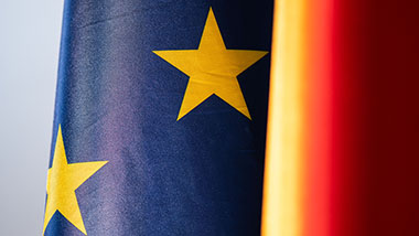 Flagge der Europäischen Union in Nahaufnahme, im Hintergrund Flagge von der Bundesrepublik Deutschland