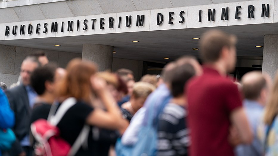 Eingang des Bundesinnenministeriums, davor unscharf eine Gruppe von Menschen