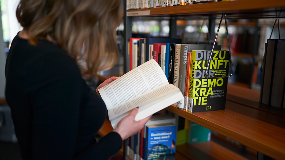 Eine Frau liest in einem aufgeschlagenen Buch vor einem Bücherregal