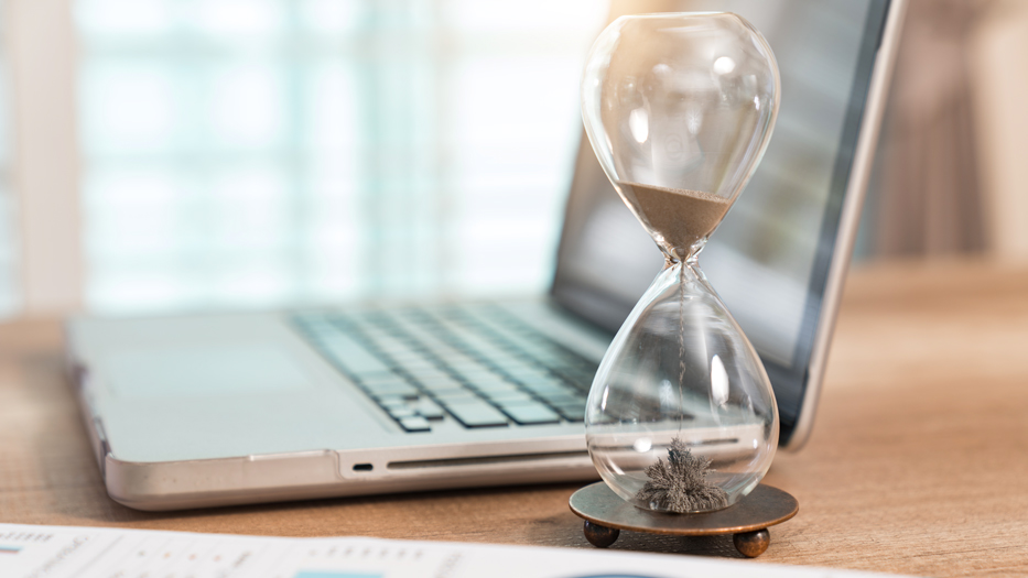 Ein Laptop und eine Sanduhr auf einem Holztisch