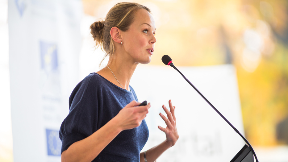 Eine Frau steht an einem Rednerpult und hält einen Vortrag