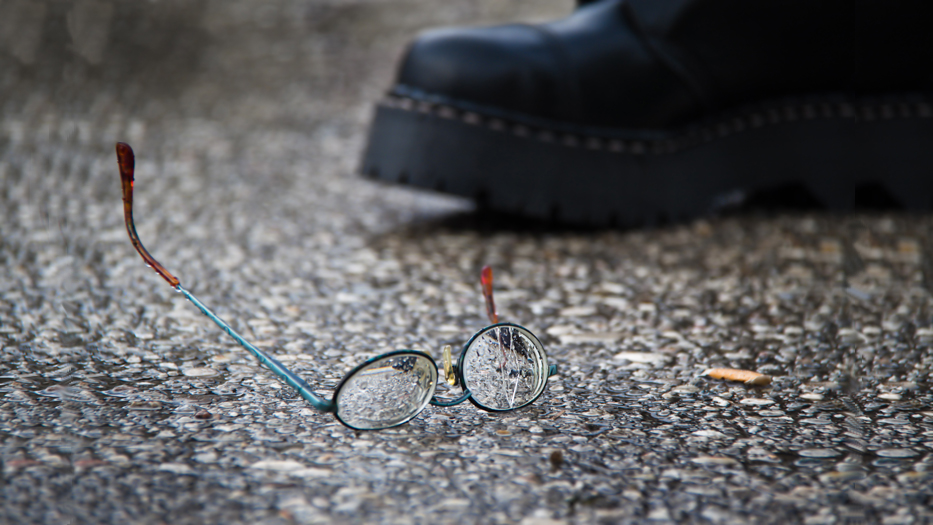Zerbrochene Brille auf der Straße neben einem Springerstiefel