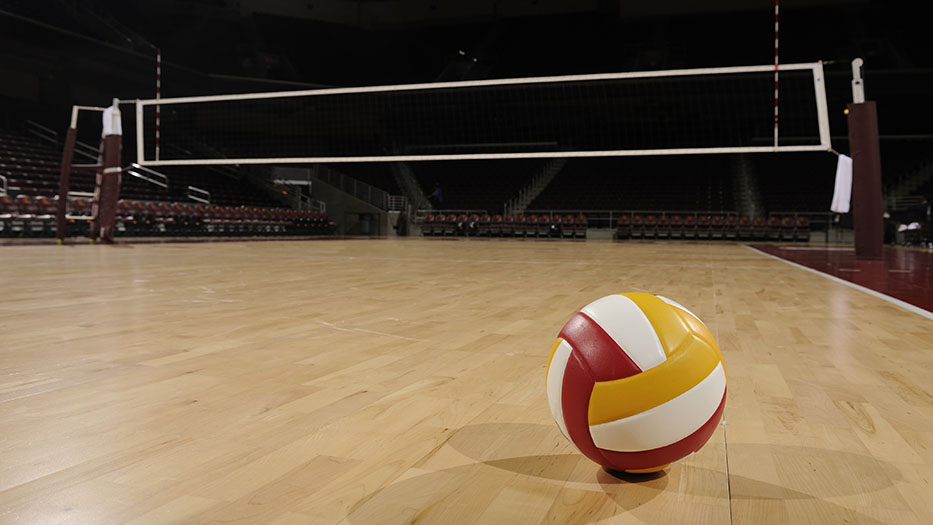 Ein Volleyball liegt auf dem Boden einer Sporthalle. Im Hintergrund das Volleyballnetz und leere Zuschauerränge