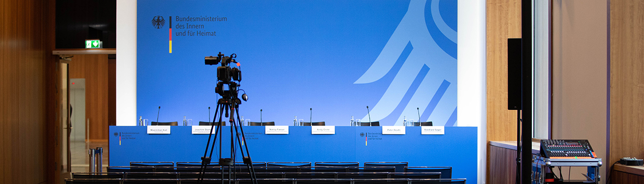 Pressekonferenztisch vor blauer Pressewand im BMI