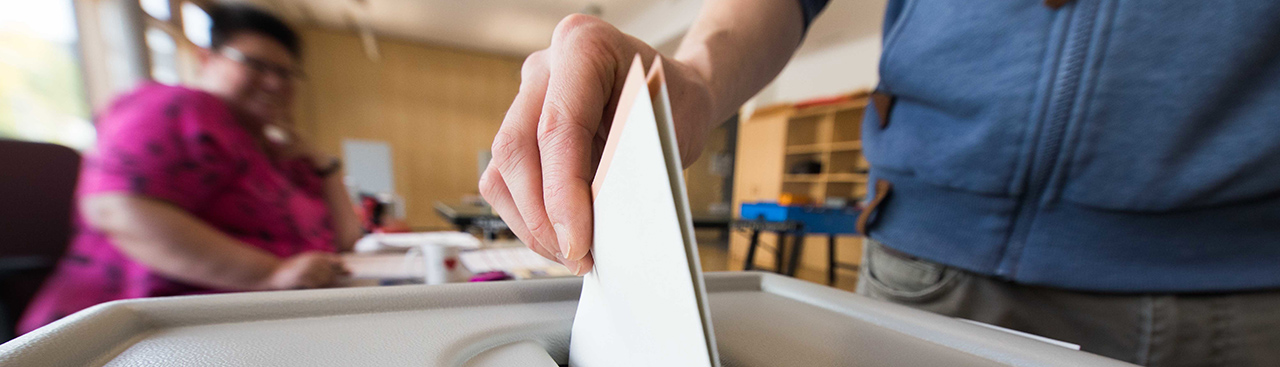 A hand throwing a ballot in a ballot box