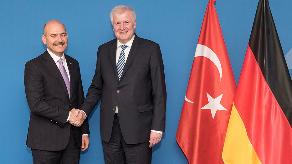 Bundesinnenminister Seehofer und S.E. Soylu stehen vor einer blauen Wand und schütteln die Hände. Daneben stehen die türkische und die deutsche Flagge.